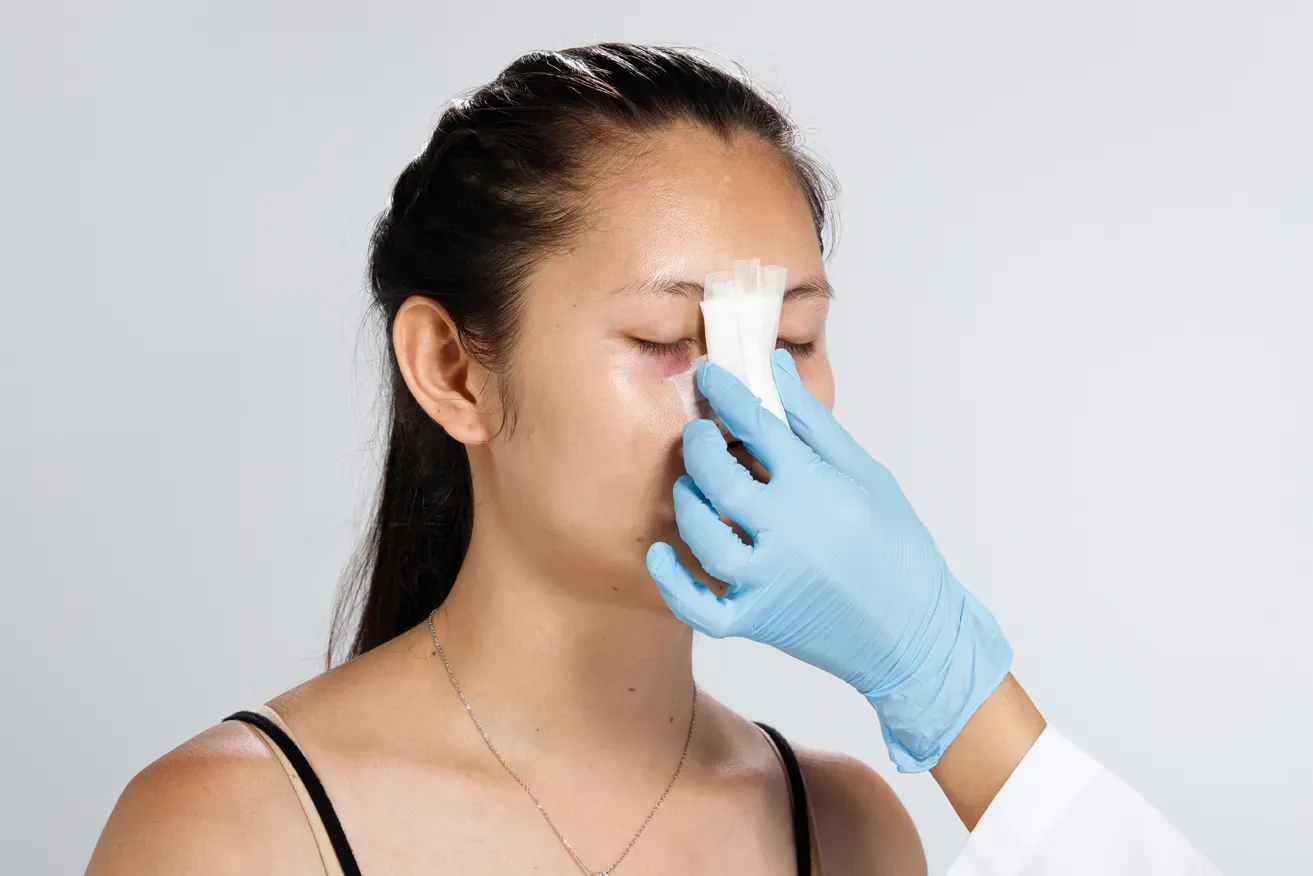 Plastic surgeon holding woman’s bandaged nose after rhinoplasty