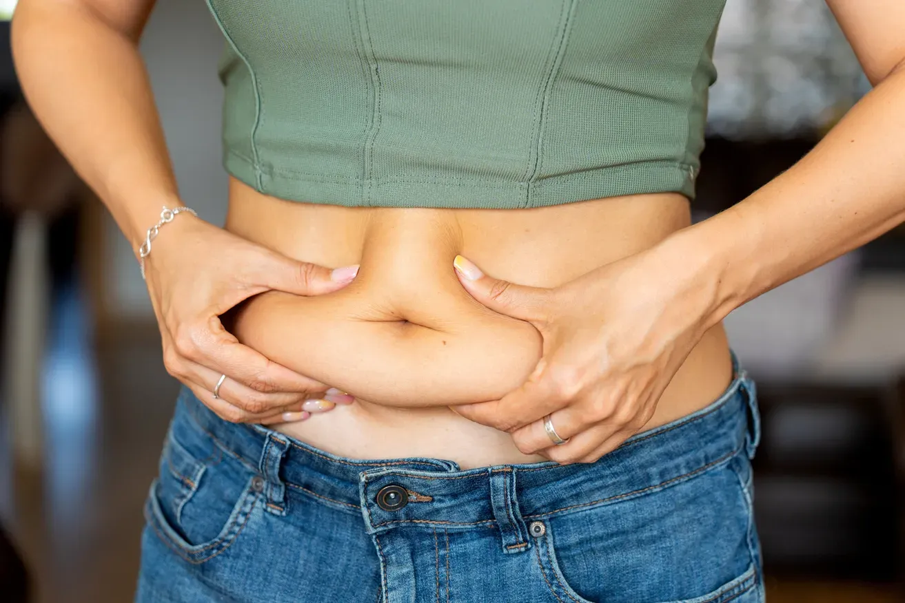Woman pinching the skin and fat around her abdomen while assessing stubborn belly fat