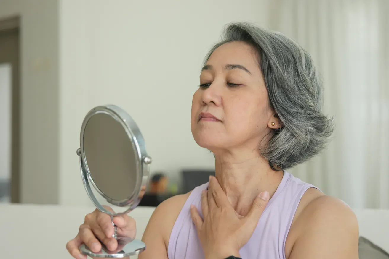 Woman looking in a mirror while assessing changes to her face following previous cosmetic surgery