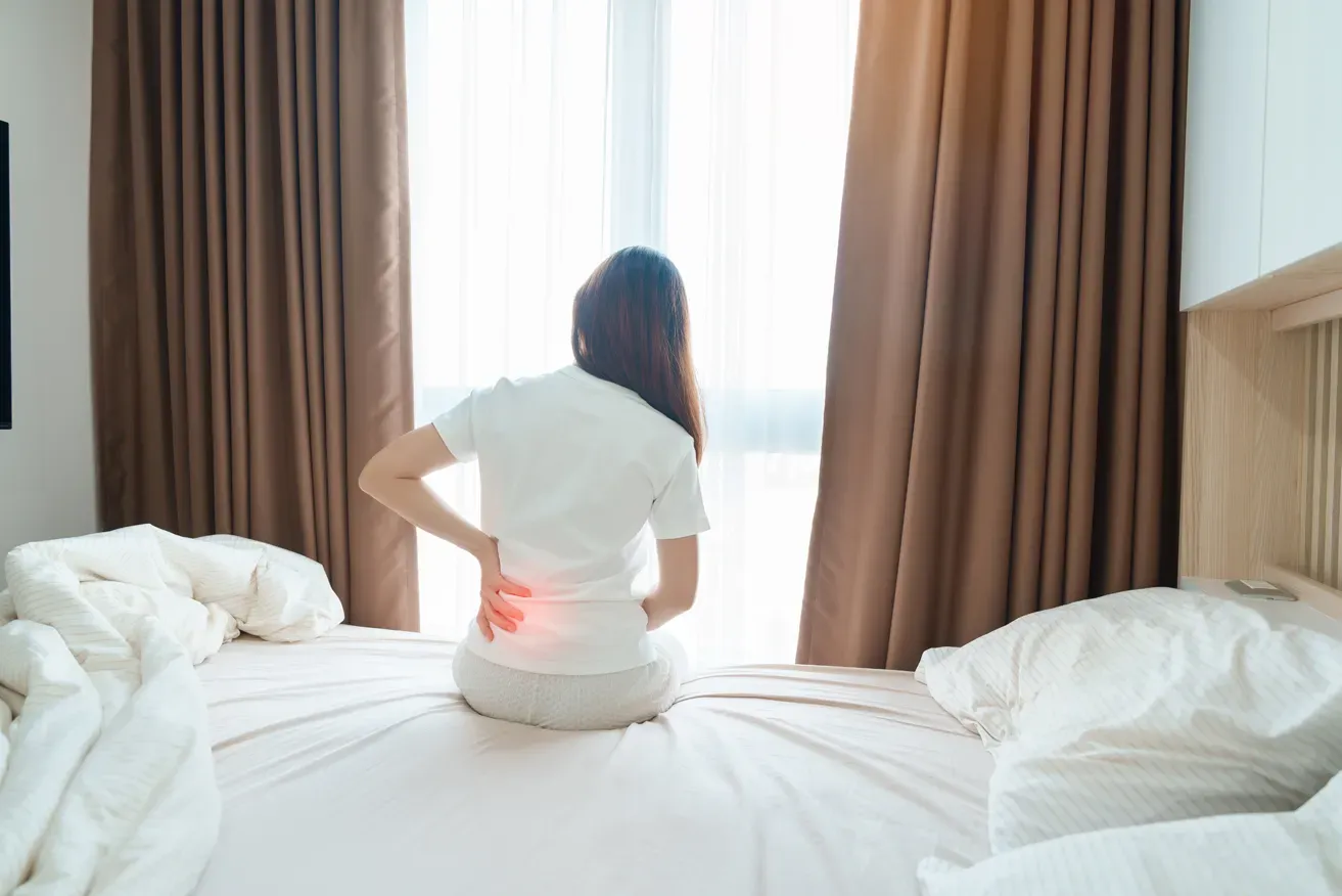 Woman experiencing back pain from large breasts after waking up