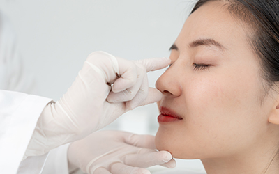 Surgeon assessing a woman’s nose during a revision rhinoplasty consultation.