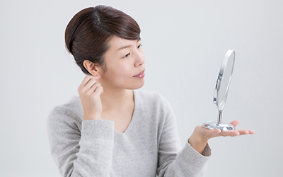 Woman examining her ears in the mirror, showing concern about uneven ear shape.