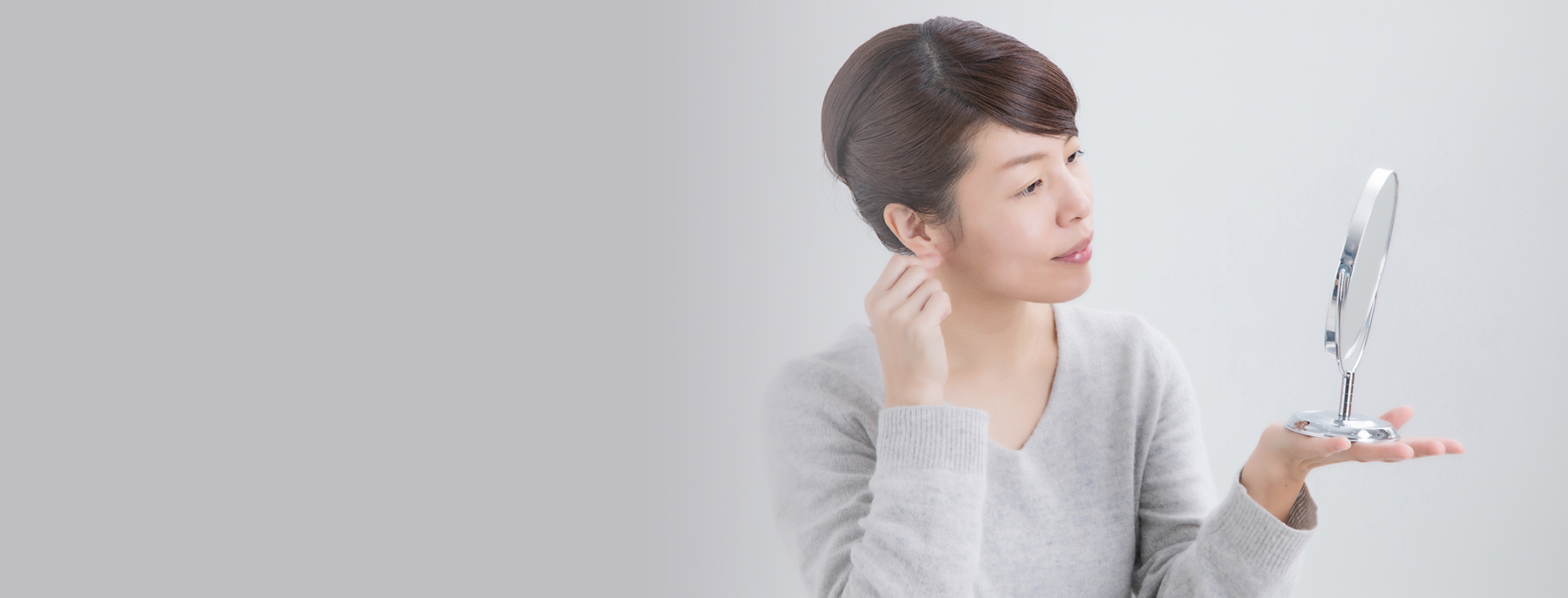 Woman examining her ears in the mirror, showing concern about uneven ear shape.