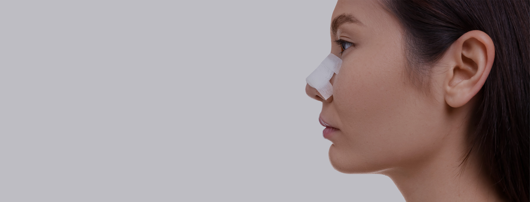Woman with a protective bandage on her nose during recovery after plastic surgery.