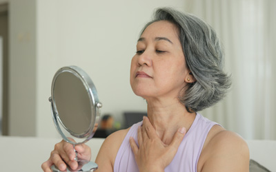 Woman looking in a mirror while assessing changes to her face following previous cosmetic surgery.