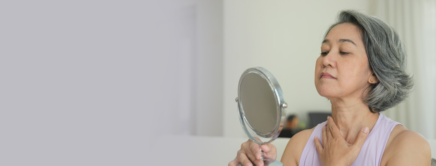 Woman looking in a mirror while assessing changes to her face following previous cosmetic surgery.